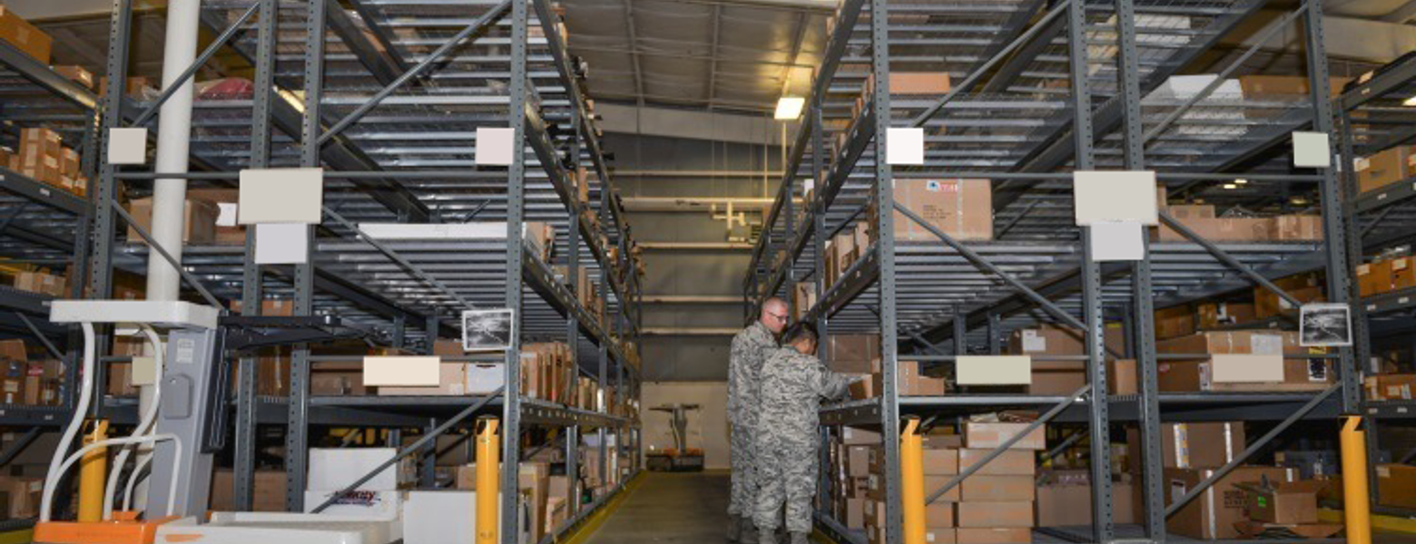 A service member standing between tall racks in a military supply warehouse