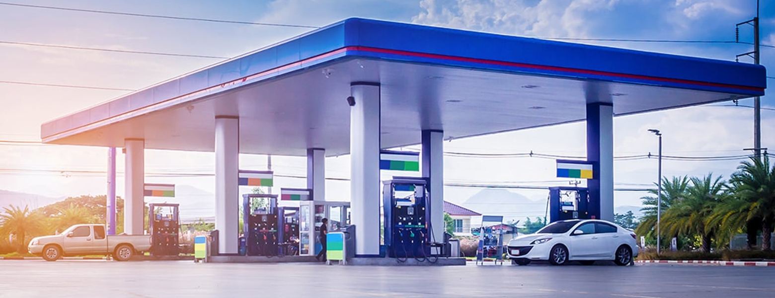 An empty filling station forecourt under its canopy, with a car parked at the edge