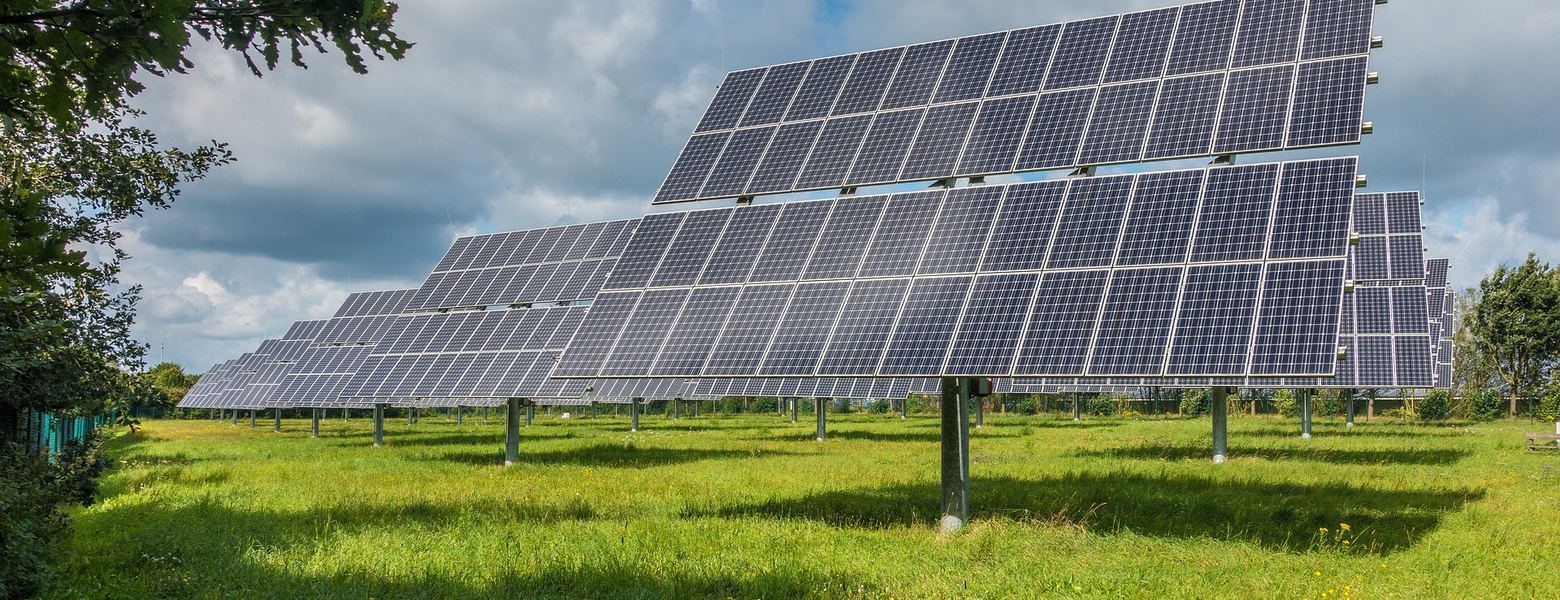 Rows of solar panels in a grass field under a partly cloudy sky