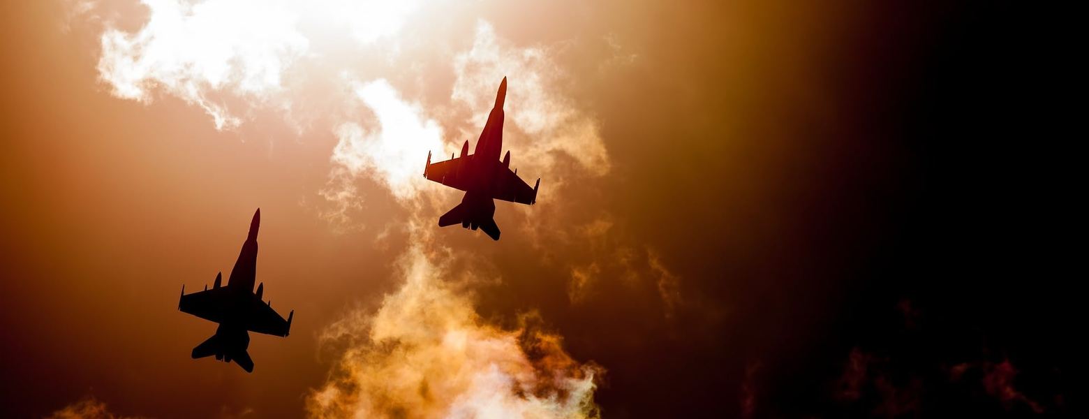 Two fighter jets silhouetted against billowing fire and smoke