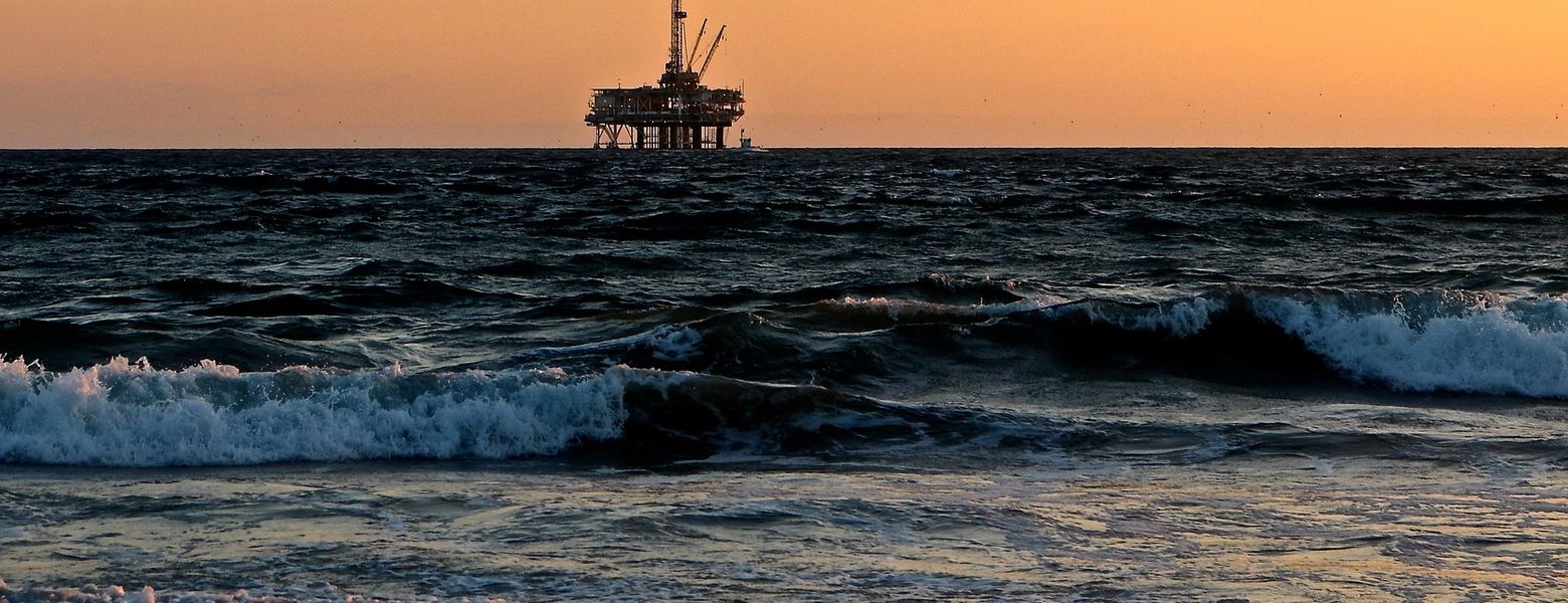 An offshore platform on the horizon beyond breaking surf at dusk