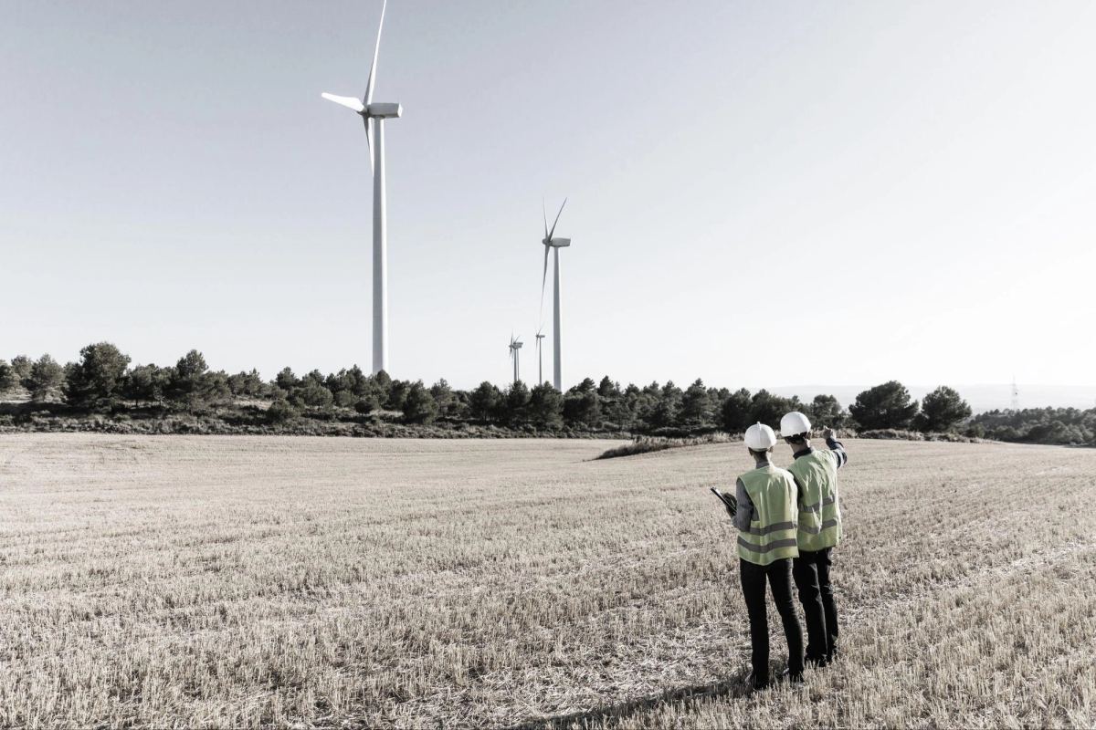 Two field engineers below a line of wind turbines