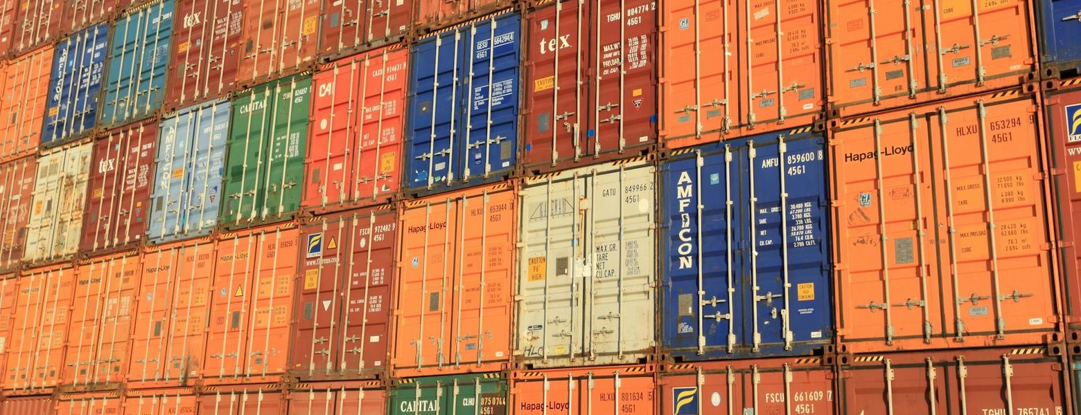 A wall of stacked shipping containers in a port yard