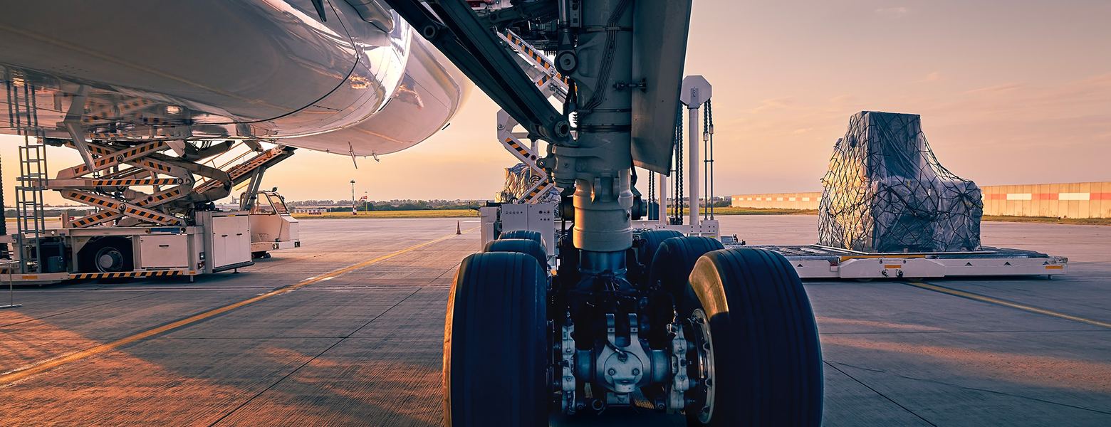 The main landing gear of a parked airliner on an airport apron at sunset