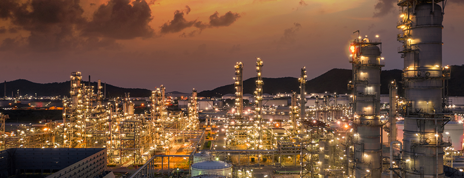 A refinery lit up at dusk under an orange sky