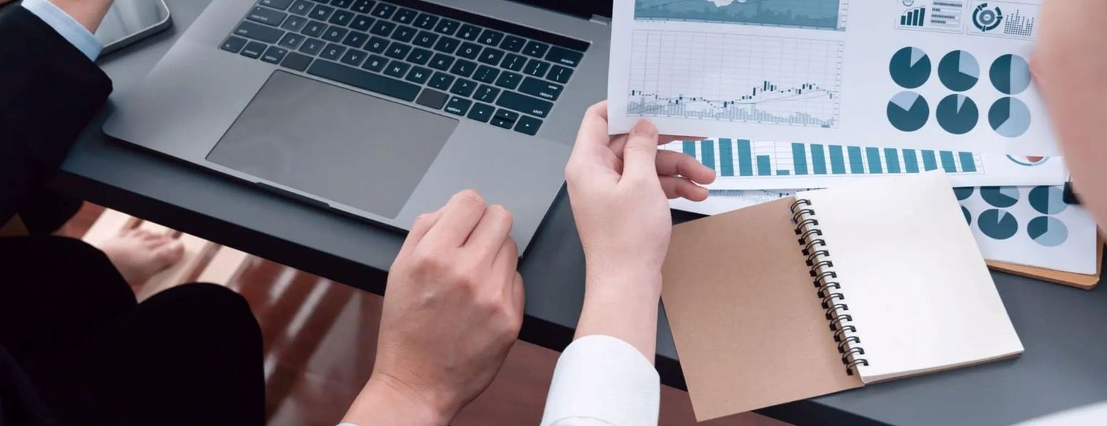 Colleagues around a table comparing printed charts beside a laptop