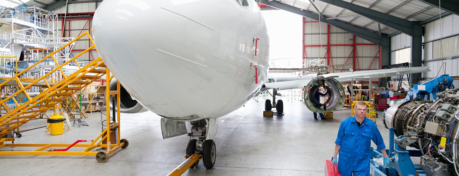 An aircraft on jacks in a maintenance hangar with an engineer walking past