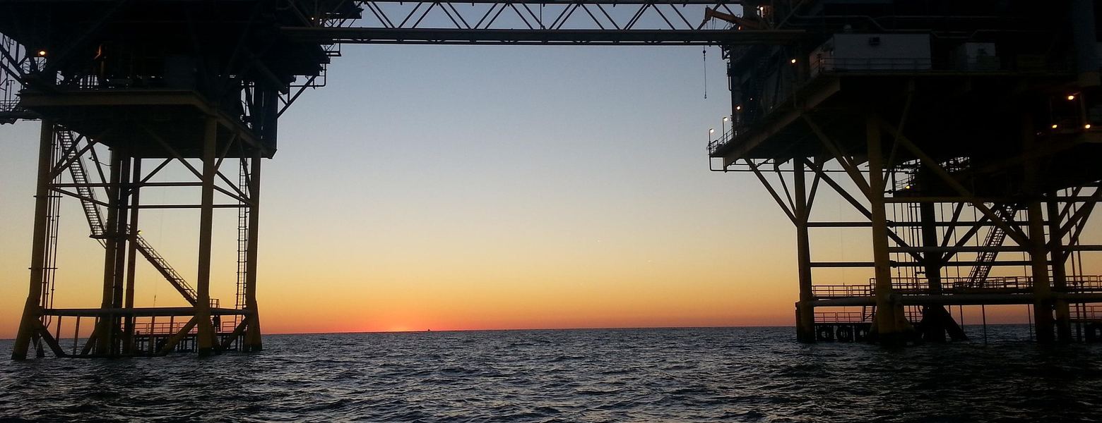 Two offshore platforms linked by a bridge, silhouetted at sunset