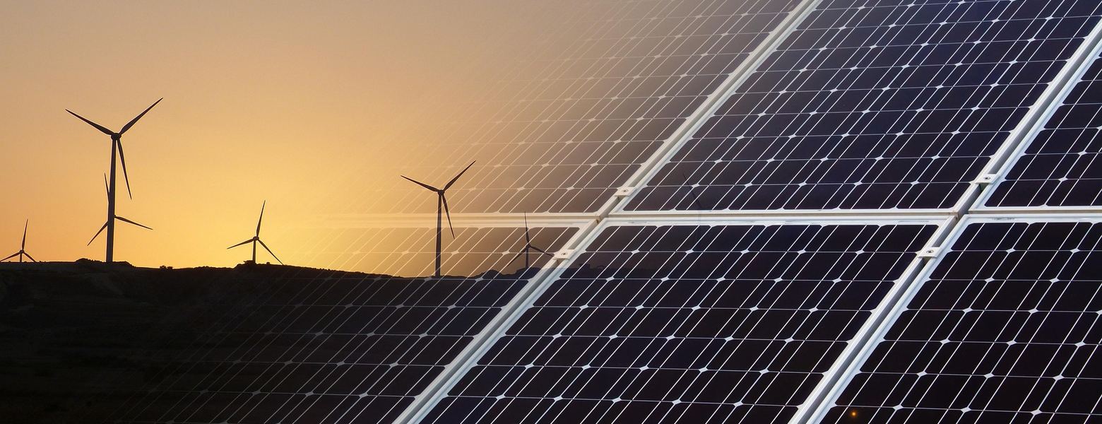 Solar panels in the foreground and wind turbines on the ridge behind, at sunset