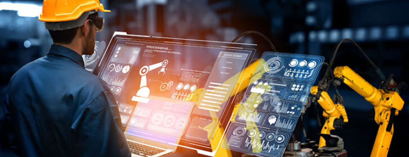 An engineer in a hard hat working across holographic dashboards beside a robotic arm