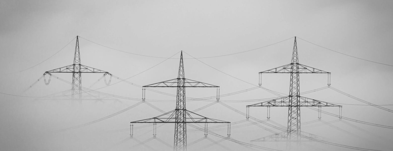 Electricity transmission pylons and power lines fading into fog