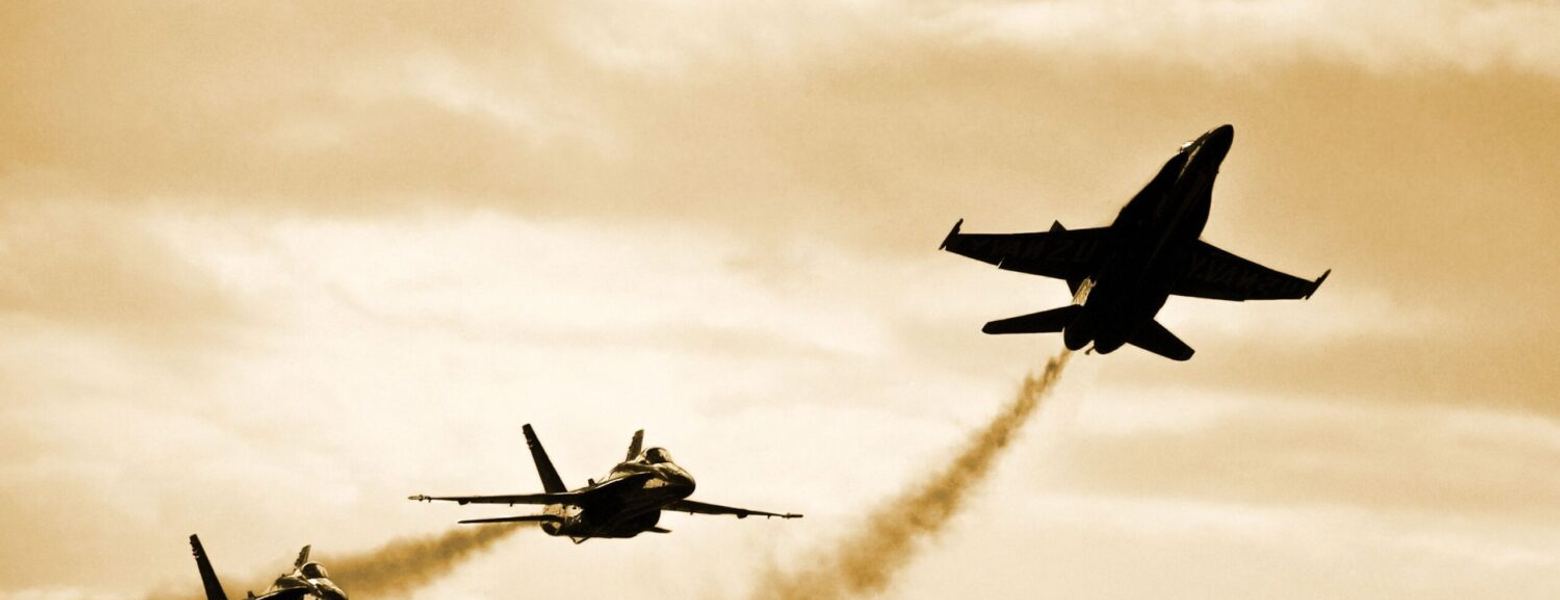 Four fighter jets flying in formation, trailing smoke against a hazy sky