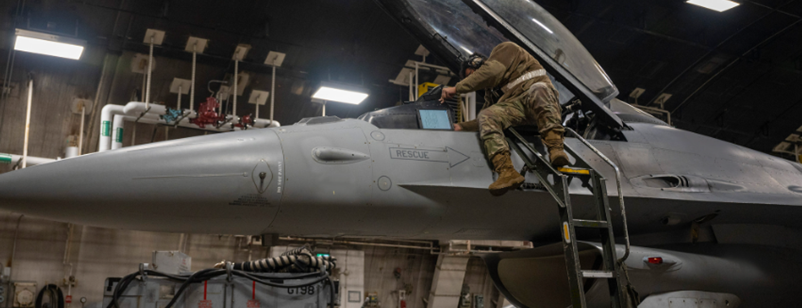 A technician working on a fighter jet in a hangar at night