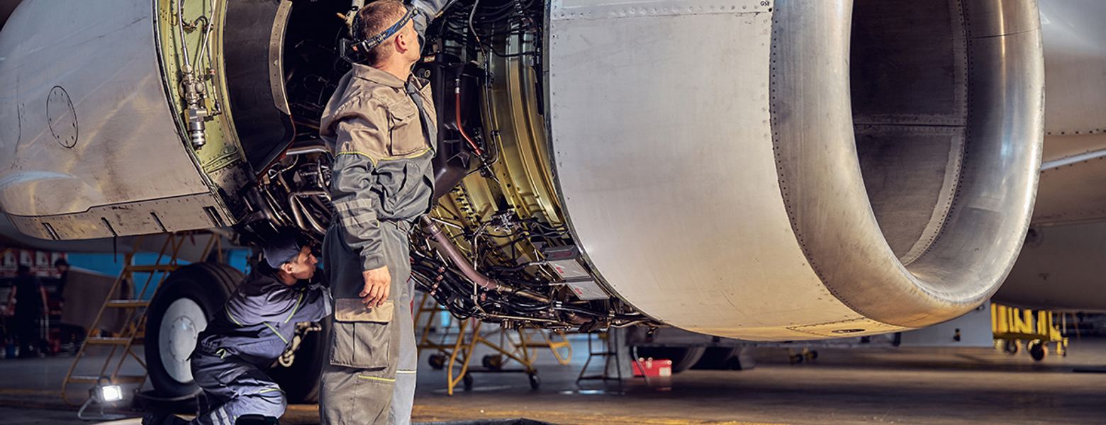 Technicians working on an open jet engine in a maintenance bay