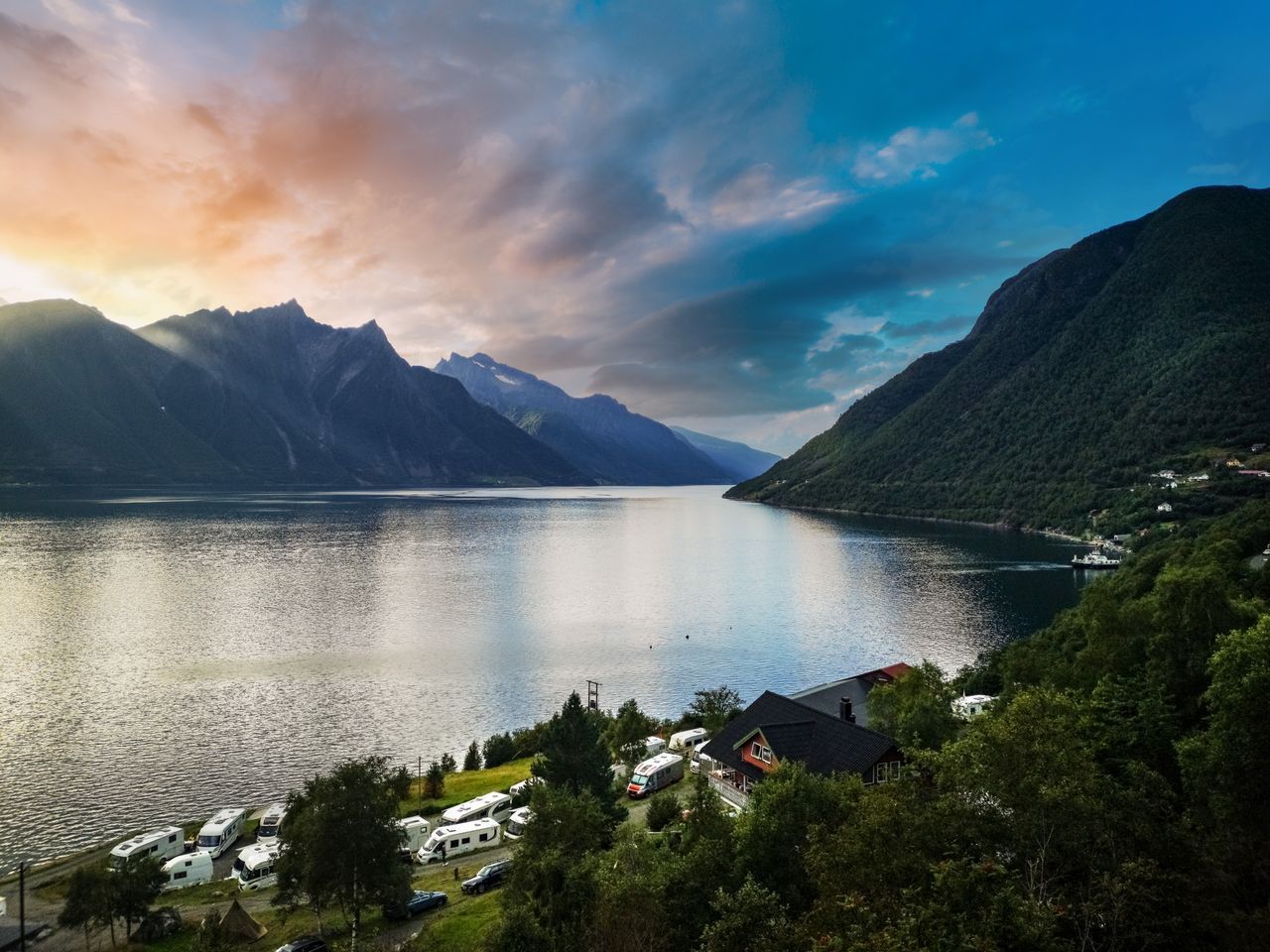 Bilde av en fjord i Norge med skyer, fjell og hus i forgrunnen