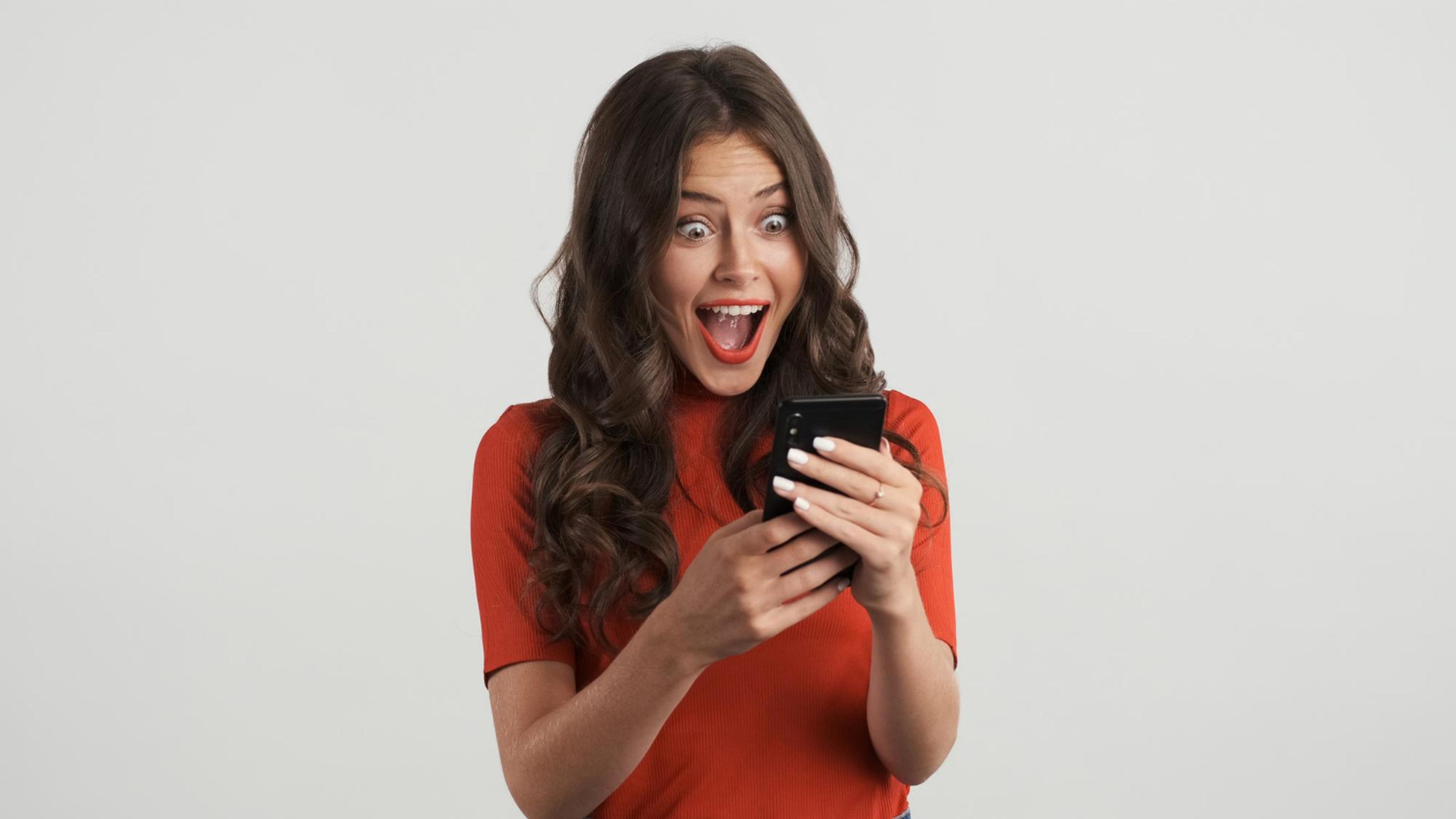 Dame som smiler og er overrasket over noe på telefonen