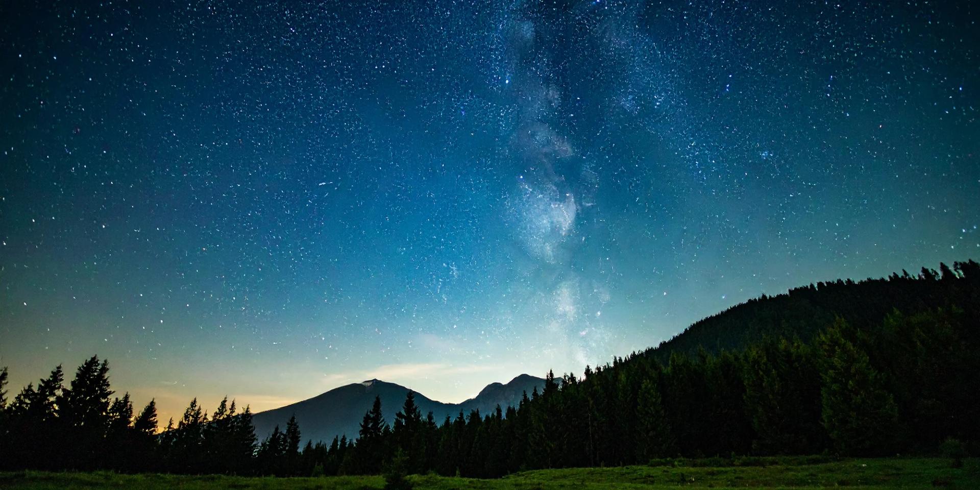 Milky Way arching over forested mountains in a starry night sky