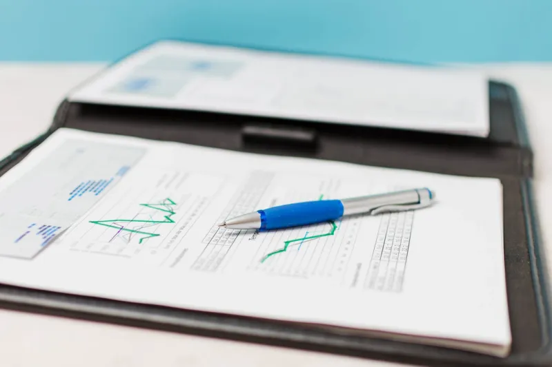 En tilstandsrapport med grafer og tabeller ligger på et skrivebord med en blå penn plassert oppå dokumentet