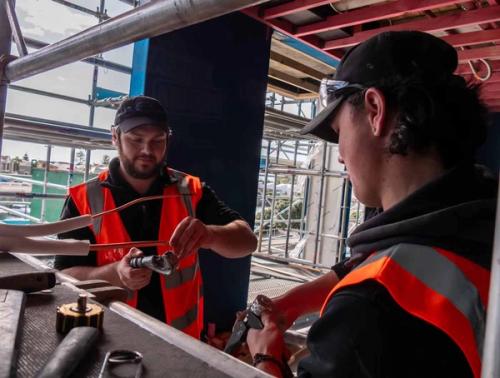 Refrigeration and air-conditioning apprentices installing pipework and fittings on a commercial HVAC job site