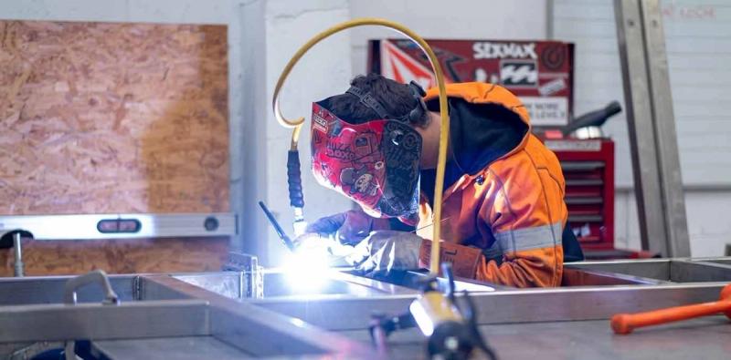 Fabrication apprentice welding a metal frame during workplace-based engineering training