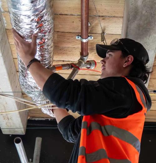 HVAC apprentice installing insulated ducting and pipework on a refrigeration and air-conditioning job site