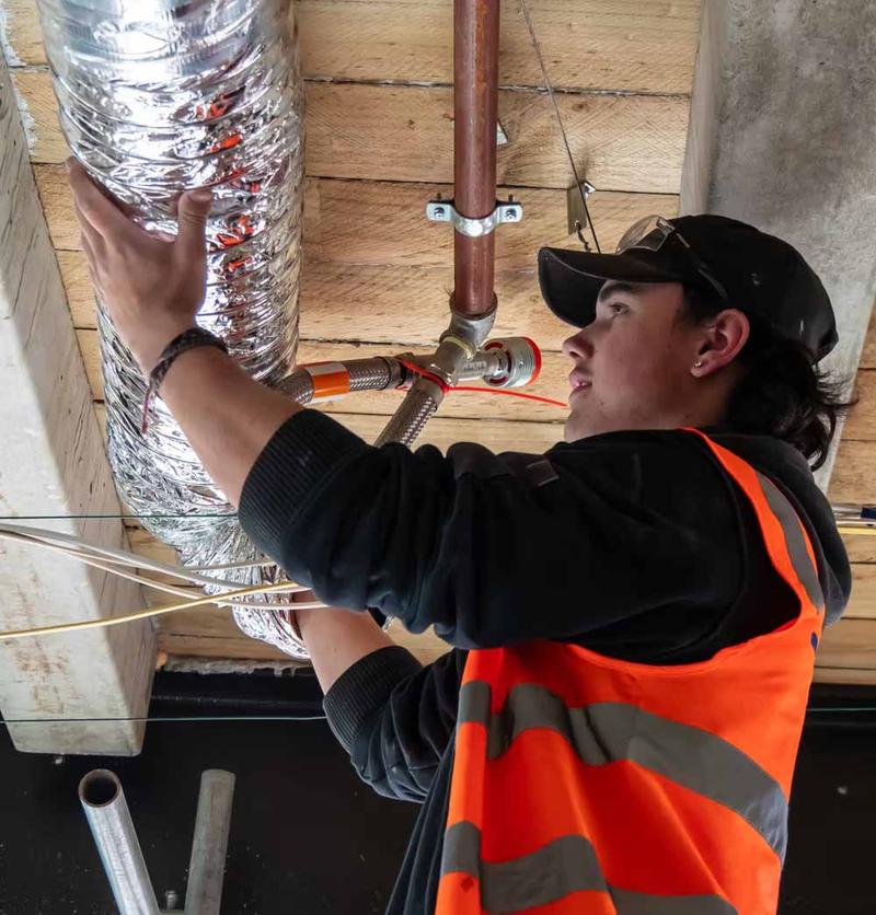 HVAC apprentice installing insulated ducting and pipework on a refrigeration and air-conditioning job site