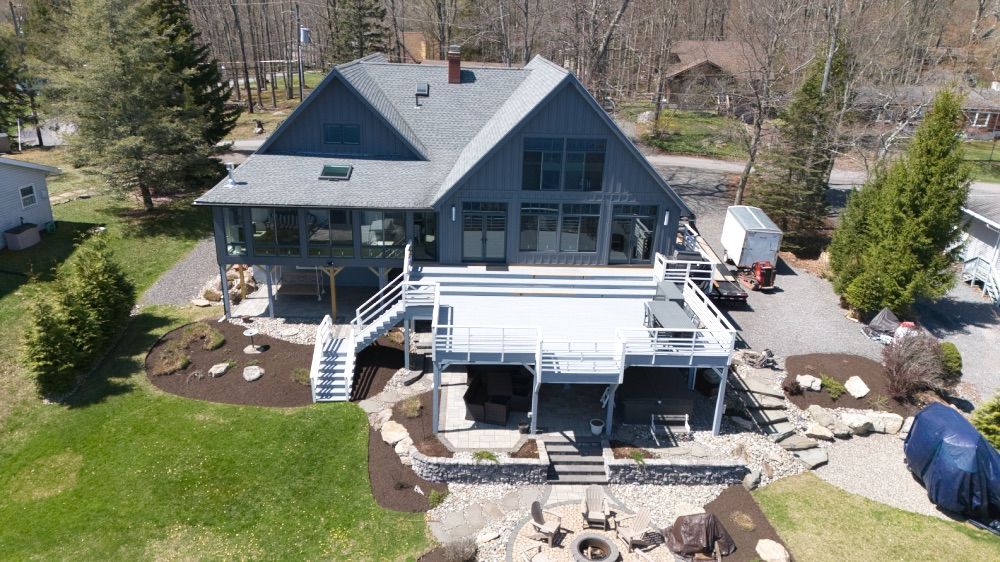 Aerial view of a renovated lakefront home in the Pocono Mountains with a multi-level deck and stone landscaping