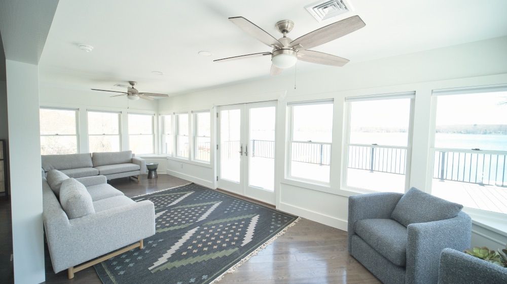 Bright sunroom with ceiling fans and floor-to-ceiling windows facing the water