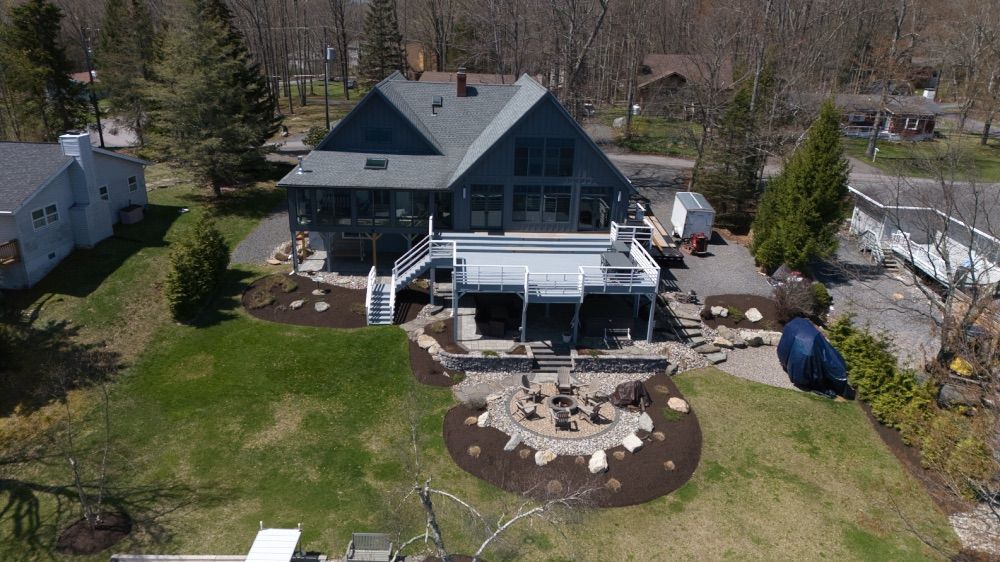 Aerial view of the lakefront property showing the home, multi-level decks, fire pit, and landscaped grounds