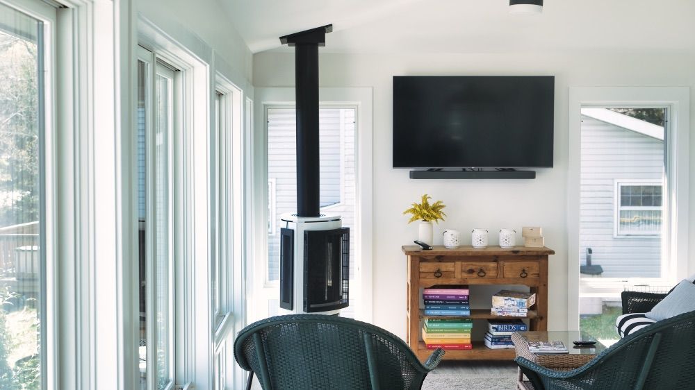 Sunroom with a wood stove, wicker chairs, and walls of glass on three sides