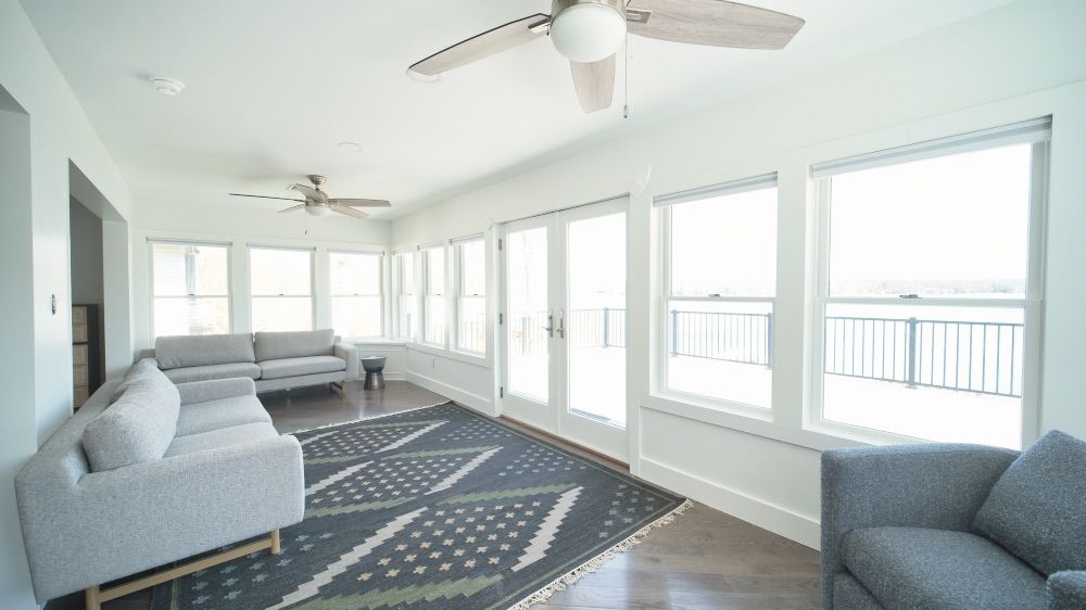 Long sunroom living space with comfortable seating, a patterned rug, and lake views