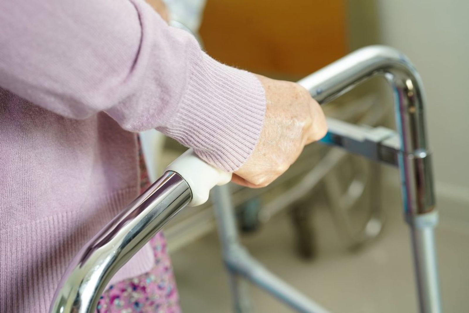 Close-up van de hand van een oudere vrouw op het handvat van een rollator.