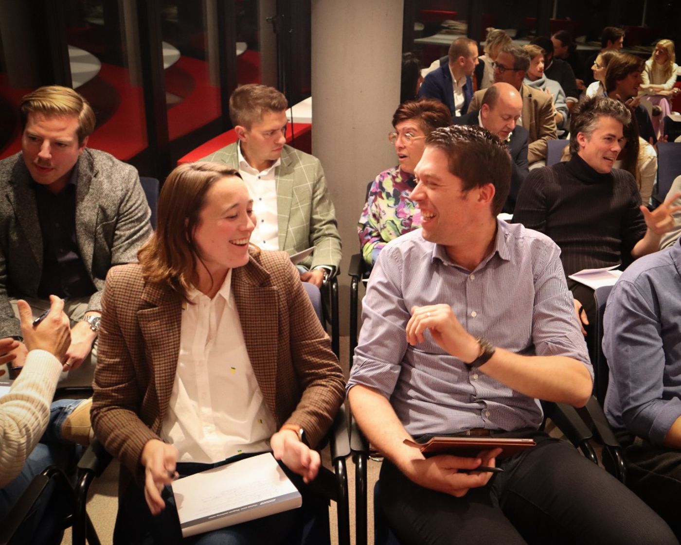 Spreker richt zich tot een aandachtig publiek van ondernemers tijdens een Ingenix-sessie in een lichte zaal met grote ramen.