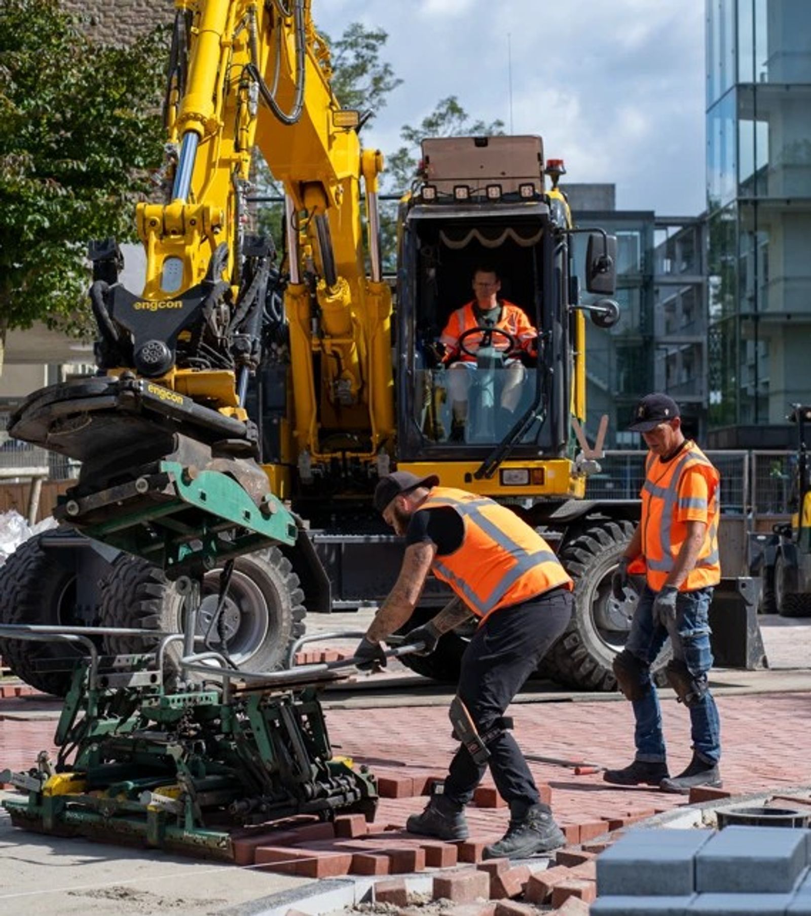 Medewerkers van Veldt Infra leggen machinaal rode klinkers met behulp van een graafmachine met legklem.