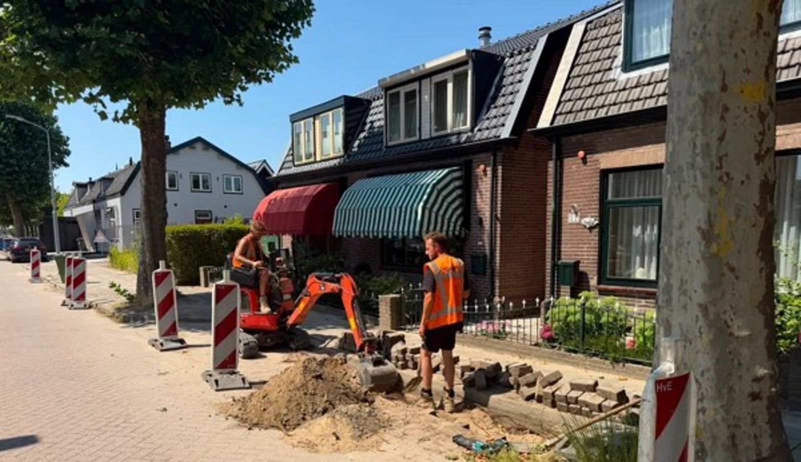 Medewerkers van Veldt Infra aan het werk met een minigraver in een woonstraat, waar de bestrating tijdelijk is opengebroken.