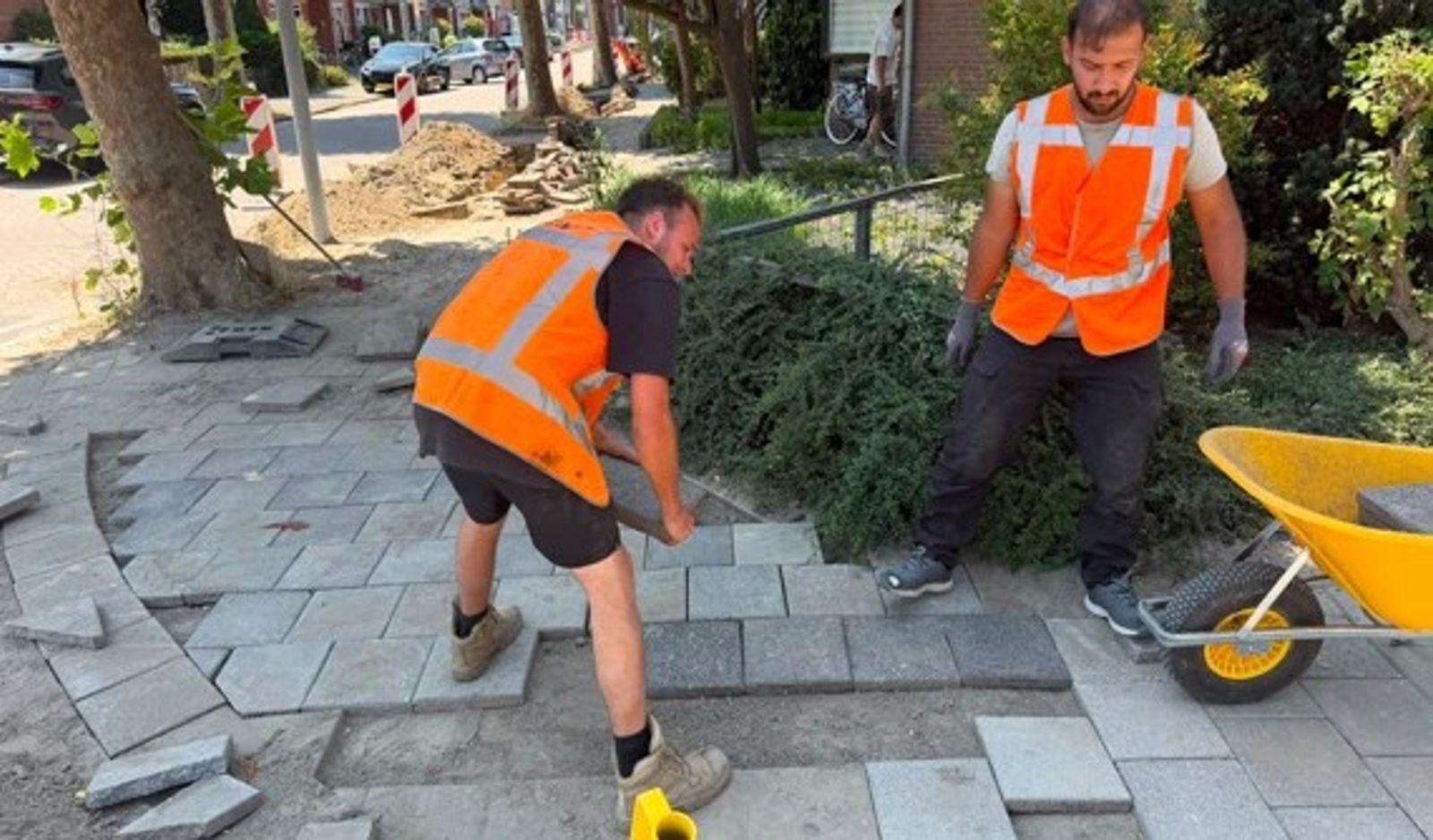 Twee stratenmakers van Veldt Infra leggen nieuwe tegels op een voetpad.