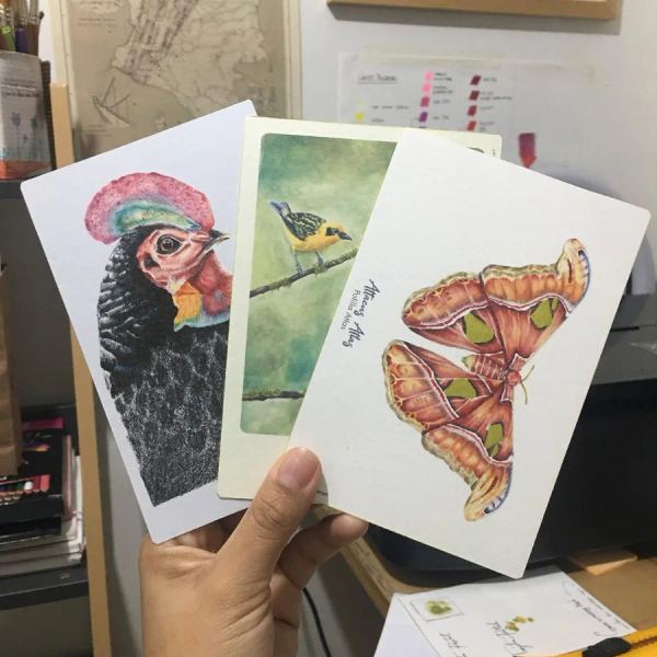 Postal ilustrada sostenida en la mano, en el taller