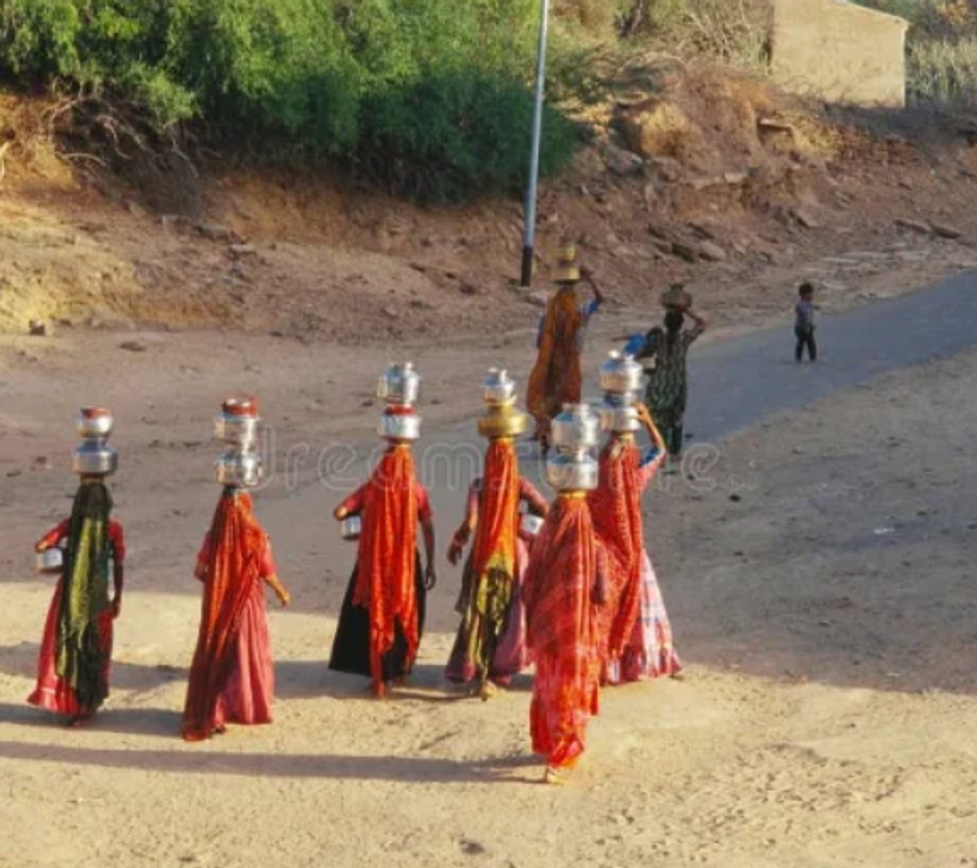 An elevated rear view of a group of women walking while carrying multiple water vessels on their heads and hips.