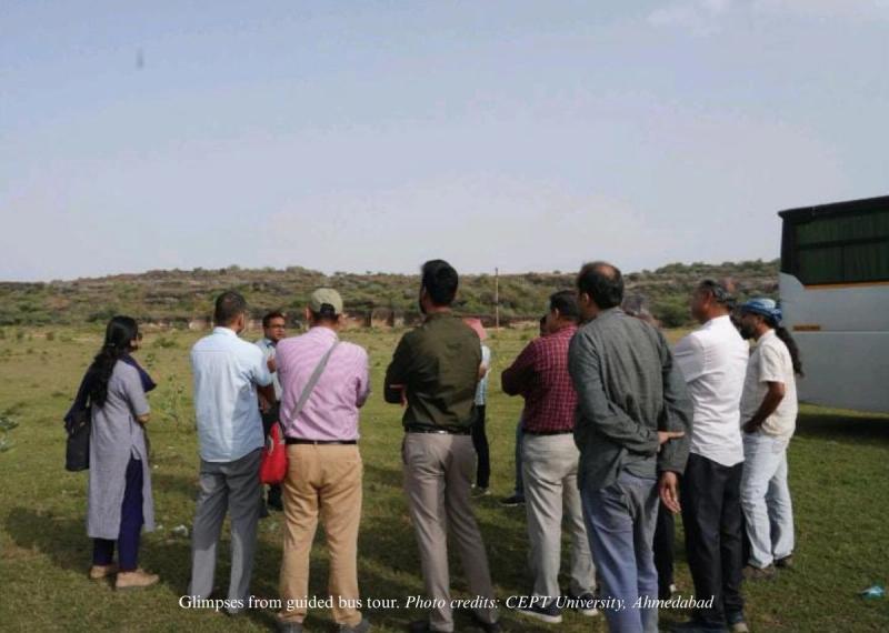 Around 10 people are standing in circle at an open ground during the bus tour.