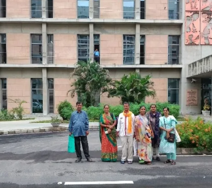 A group of 2 men and 4 women standing in front of big building.