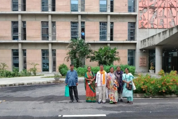 A group of 2 men and 4 women standing in front of big building.
