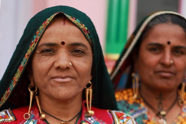 A woman in traditional colorful clothing and jewelry holds up a document written in Gujarati.