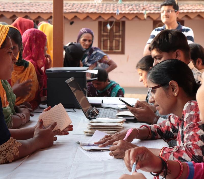 Women at a registration desk submit documents to officials during a community outreach event.
