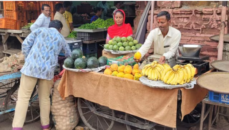 A street vendor with fruits to sell. A women standing near to him.