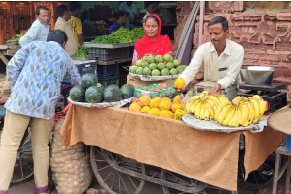 A street vendor with fruits to sell. A women standing near to him.