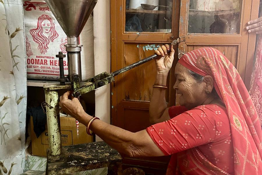 A woman wearing a red sari is filling a mehndi cone with a hand-operated machine.