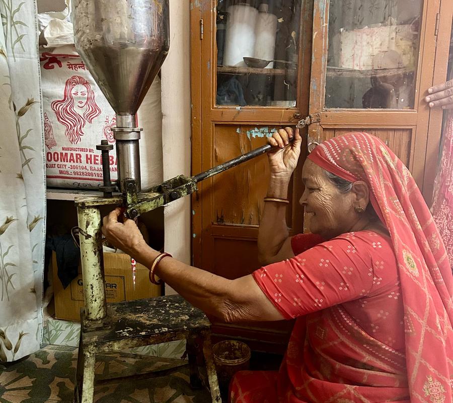 A woman wearing a red sari is filling a mehndi cone with a hand-operated machine.