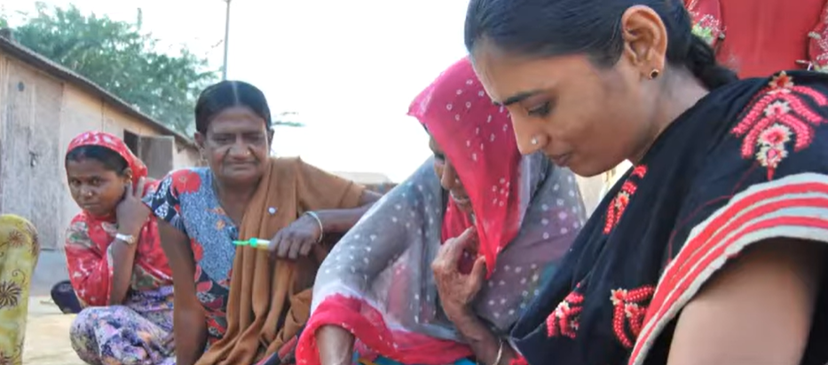 Four women sitting together on a ground and filling out a form