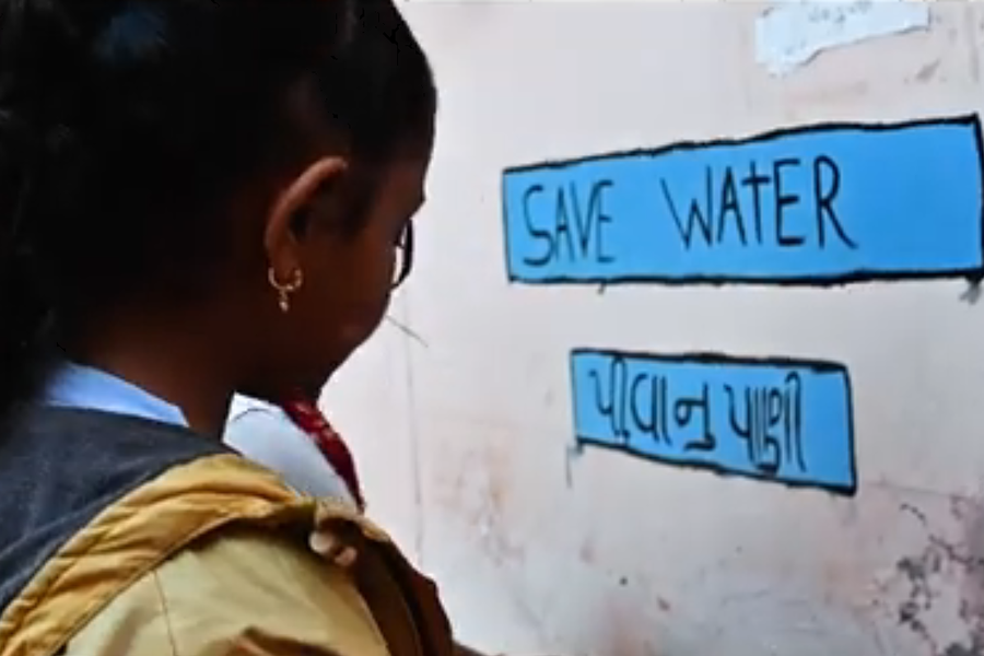 Two young girls washing their hands. A poster written "Save Water" is pasted on the wall.