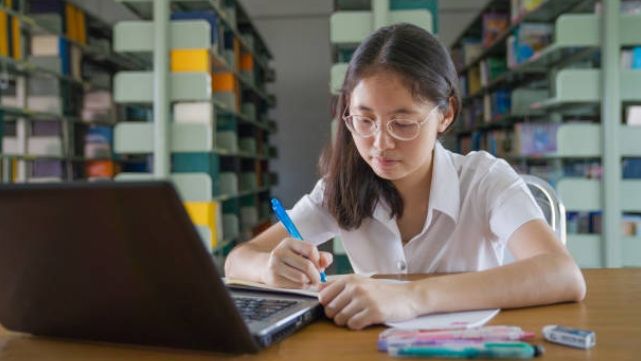 Secondary school student studying efficiently with books and laptop, applying study hacks to improve learning